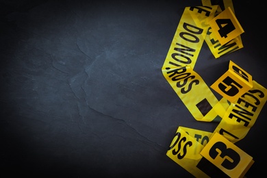 Crime scene tape and evidence markers on black slate background, flat lay. Space for text