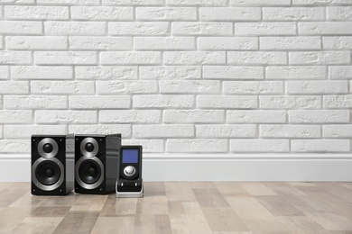 Modern powerful audio speakers and remote on floor near white brick wall. Space for text