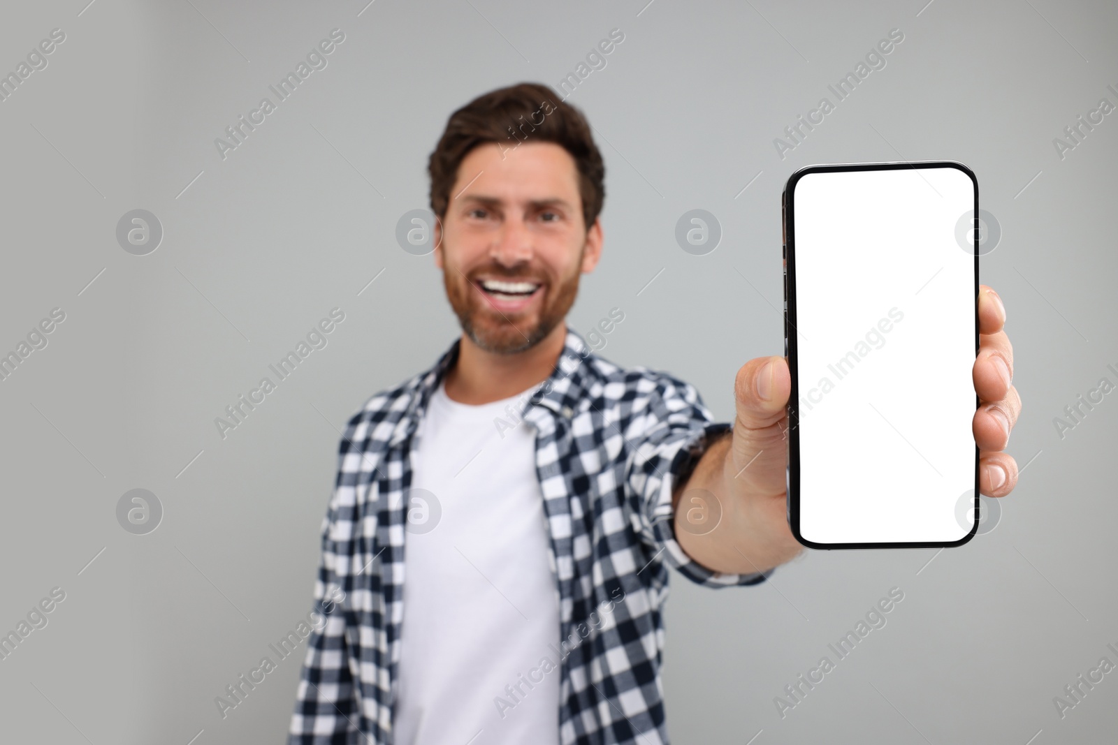 Photo of Handsome man showing smartphone in hand on light grey background, selective focus. Mockup for design