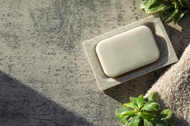 Photo of Dish with soap bar, terry towel and green plants on light grey textured table, flat lay. Space for text