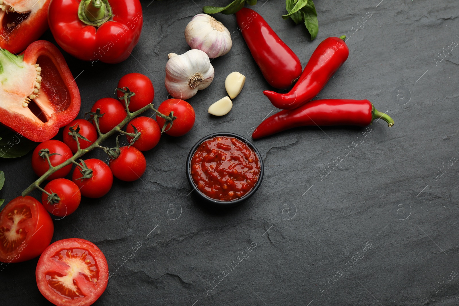Photo of Delicious adjika sauce in bowl and ingredients on black table, flat lay