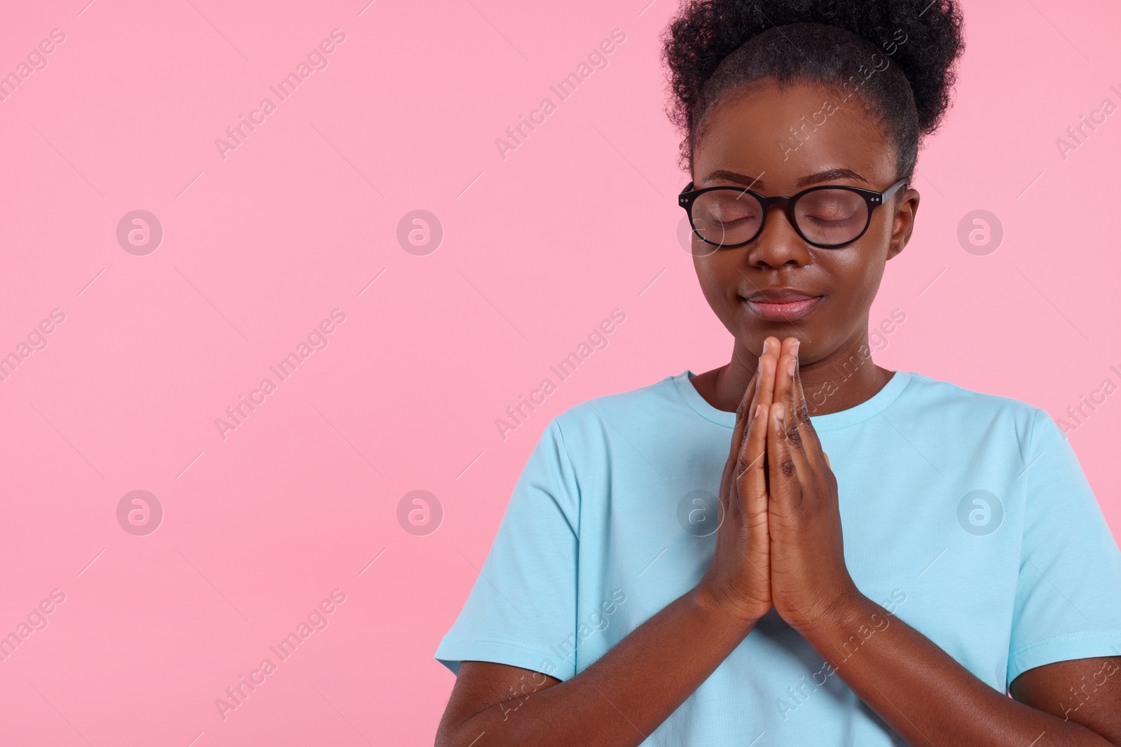 Photo of Woman with clasped hands praying to God on pink background. Space for text