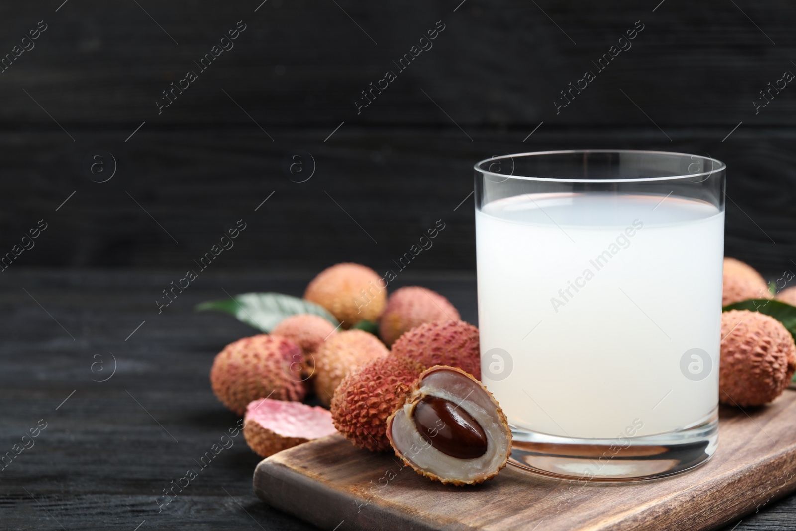 Photo of Lychee juice and fresh fruits on black wooden table. Space for text