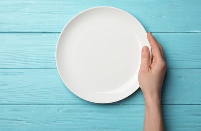 Woman with empty plate at wooden table, top view