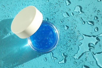 Photo of Open jar of cosmetic product on wet turquoise background, top view. Space for text