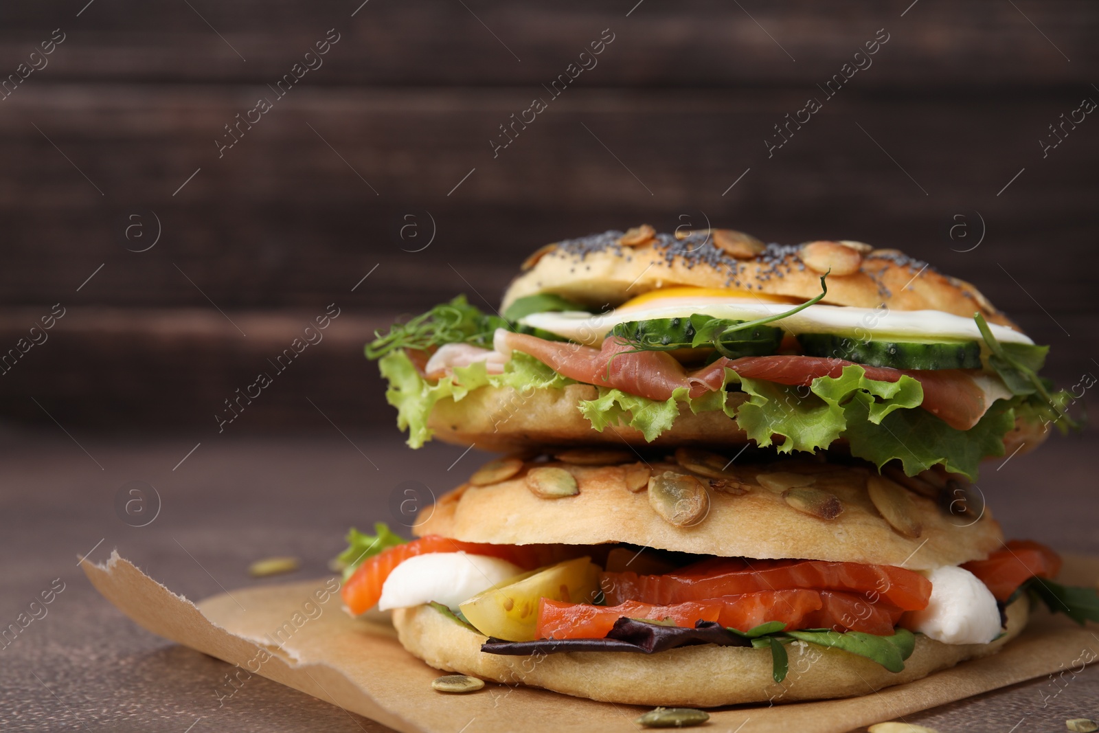 Photo of Stacked tasty bagel sandwiches on brown table, closeup. Space for text