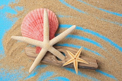 Piece of wood with beautiful starfishes, shell and sand on blue background, flat lay