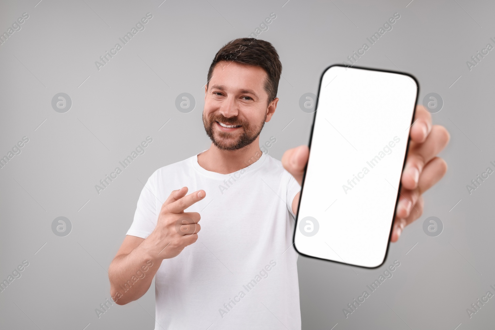 Photo of Handsome man showing smartphone in hand and pointing at it on light grey background