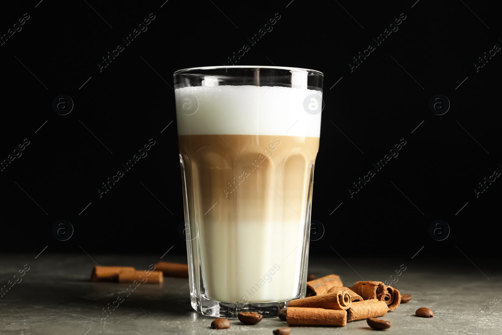 Photo of Delicious latte macchiato and cinnamon on grey table against black background