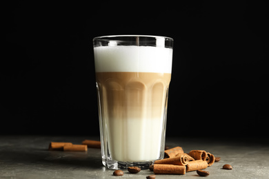 Photo of Delicious latte macchiato and cinnamon on grey table against black background