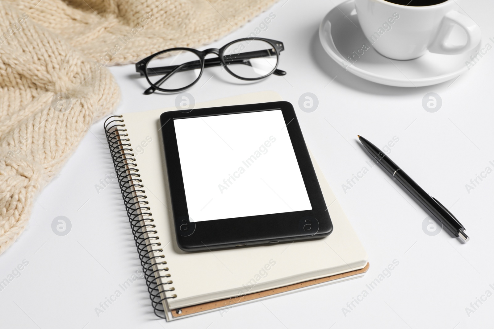 Photo of Modern e-book reader, notebook and pen on white table