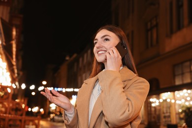 Photo of Beautiful woman talking by smartphone on night city street