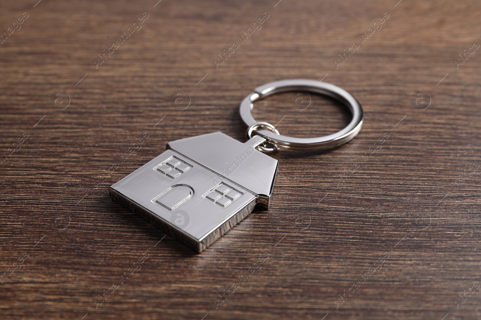Photo of Metal keychain in shape of house on wooden table, closeup