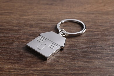 Photo of Metal keychain in shape of house on wooden table, closeup