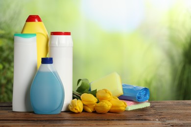 Photo of Spring cleaning. Different detergents, tools and beautiful flowers on wooden table outdoors, space for text