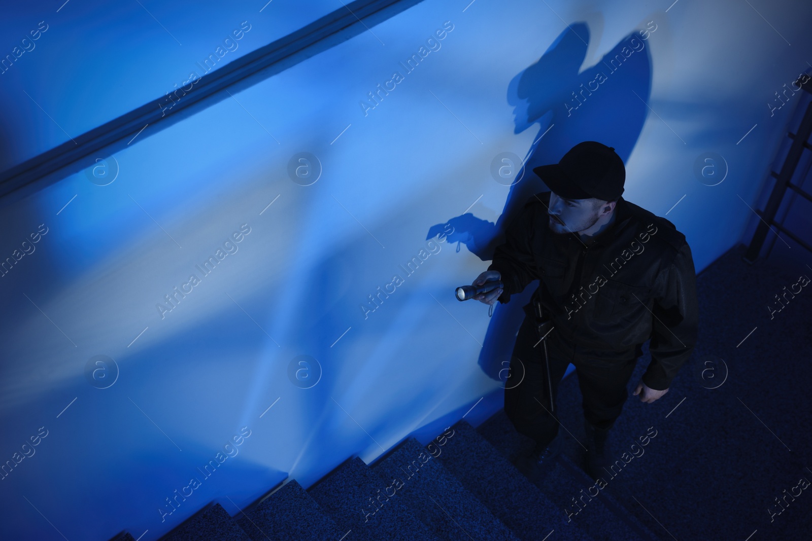 Photo of Male security guard with flashlight going up stairs in darkness