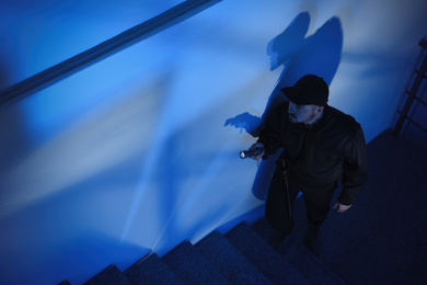Photo of Male security guard with flashlight going up stairs in darkness
