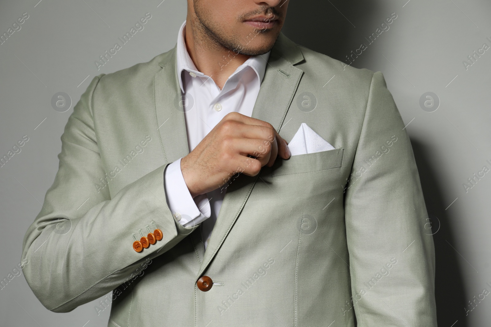 Photo of Man fixing handkerchief in breast pocket of his suit on grey background, closeup