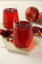 Photo of Tasty pomegranate juice in glasses and fresh fruits on white wooden table, closeup