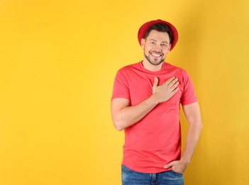 Portrait of handsome man holding hand near his heart on color background, space for text