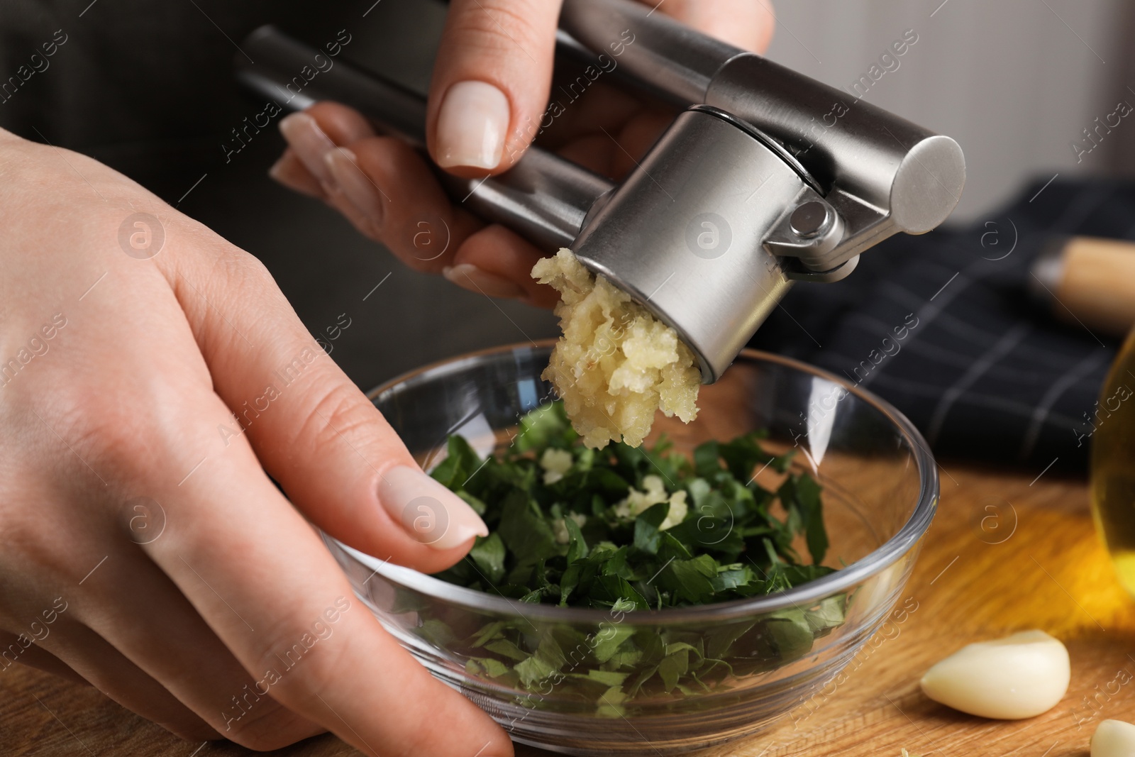 Photo of Woman squeezing garlic with press at wooden table, closeup