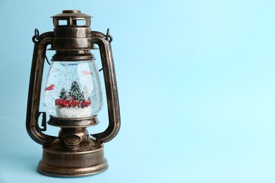 Beautiful snow globe in vintage lantern on light blue background, space for text