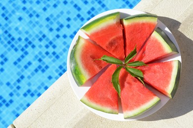 Photo of Slices of watermelon on white plate near swimming pool outdoors, top view. Space for text