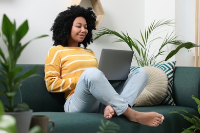 Photo of Relaxing atmosphere. Happy woman with laptop on sofa near beautiful houseplants in room