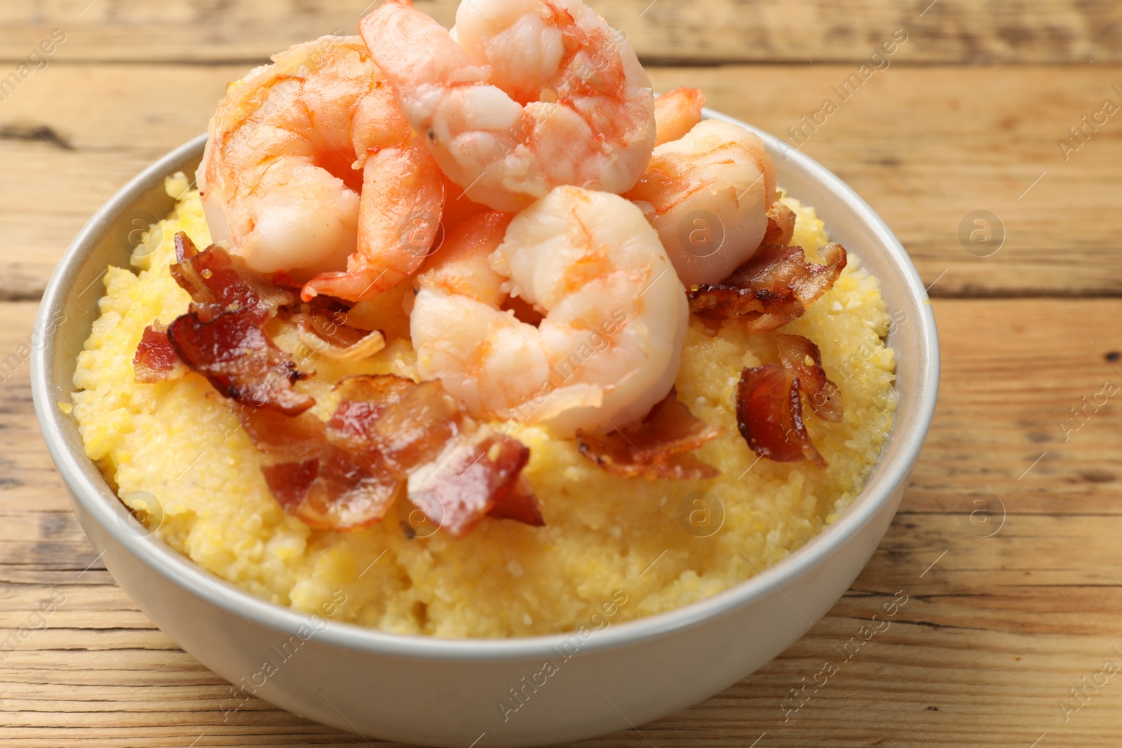 Photo of Fresh tasty shrimps, bacon and grits in bowl on wooden table, closeup