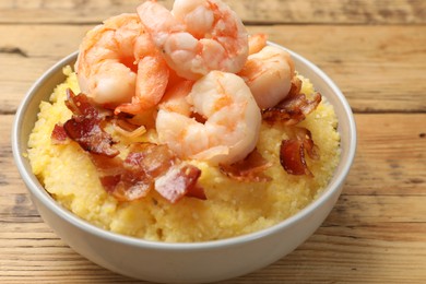 Fresh tasty shrimps, bacon and grits in bowl on wooden table, closeup