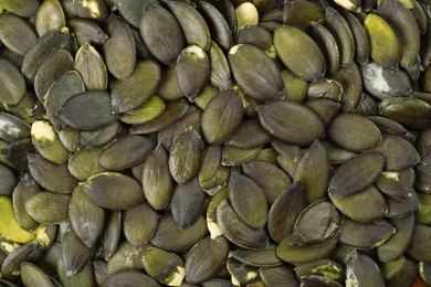 Photo of Many peeled pumpkin seeds as background, top view
