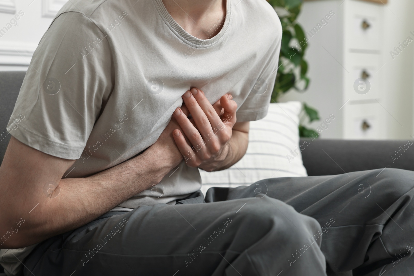 Photo of Man suffering from heart hurt on sofa at home, closeup