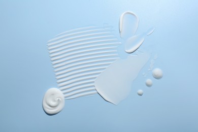 Samples of face cream on light blue background, top view