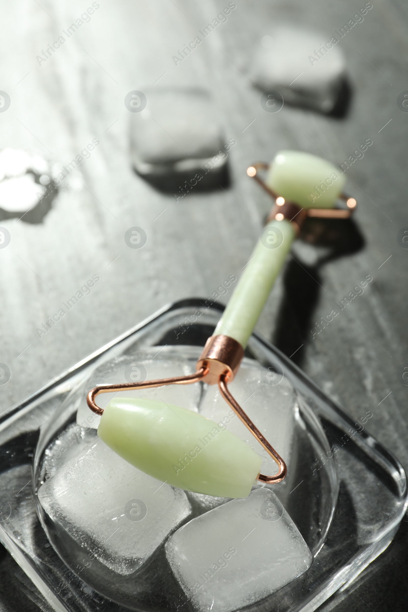 Photo of Natural jade face roller and ice cubes on grey background, closeup