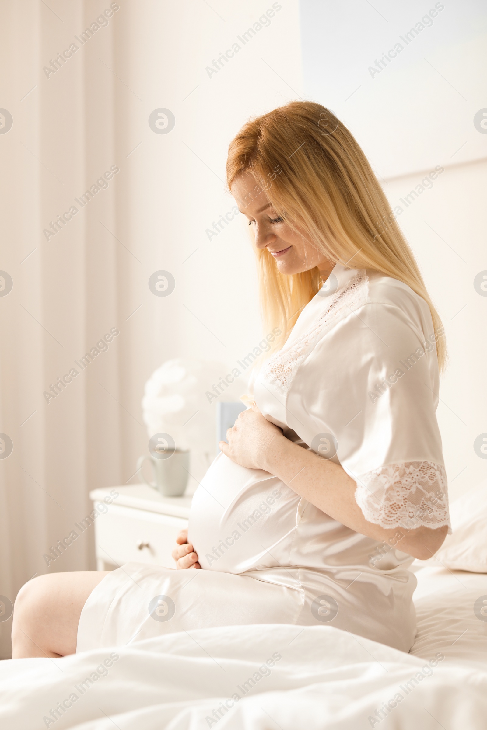 Photo of Beautiful pregnant woman sitting on bed in light room