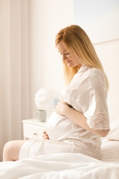 Photo of Beautiful pregnant woman sitting on bed in light room