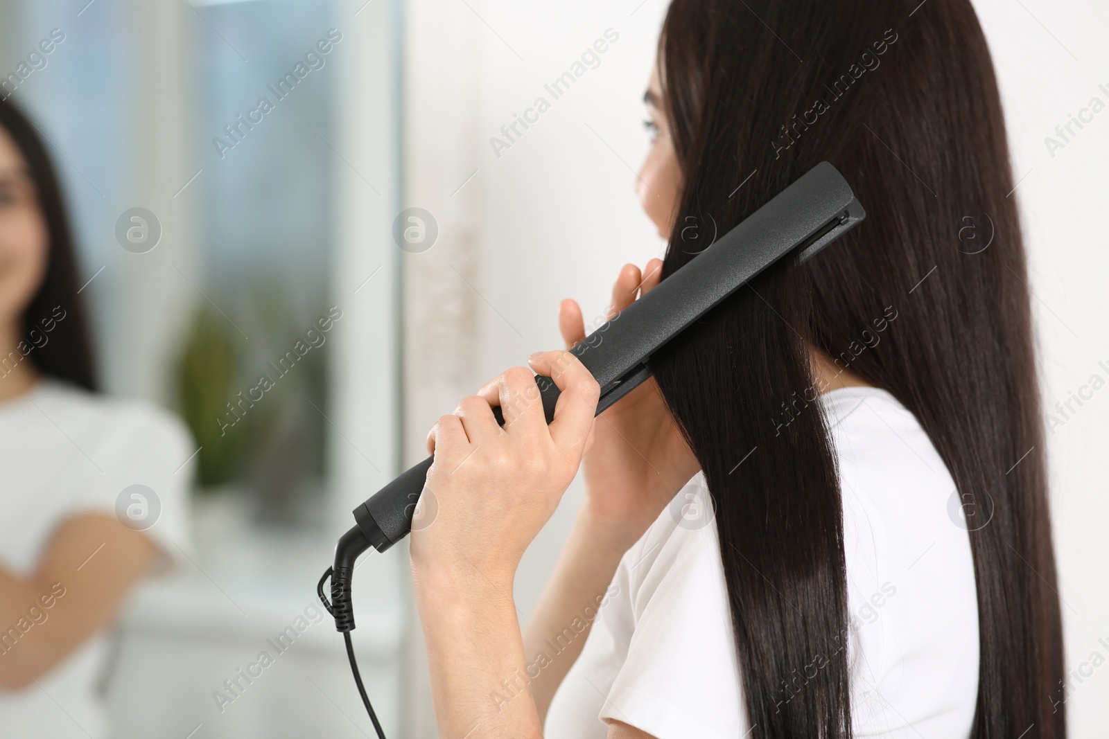Photo of Woman using hair iron near mirror in room, closeup. Space for text