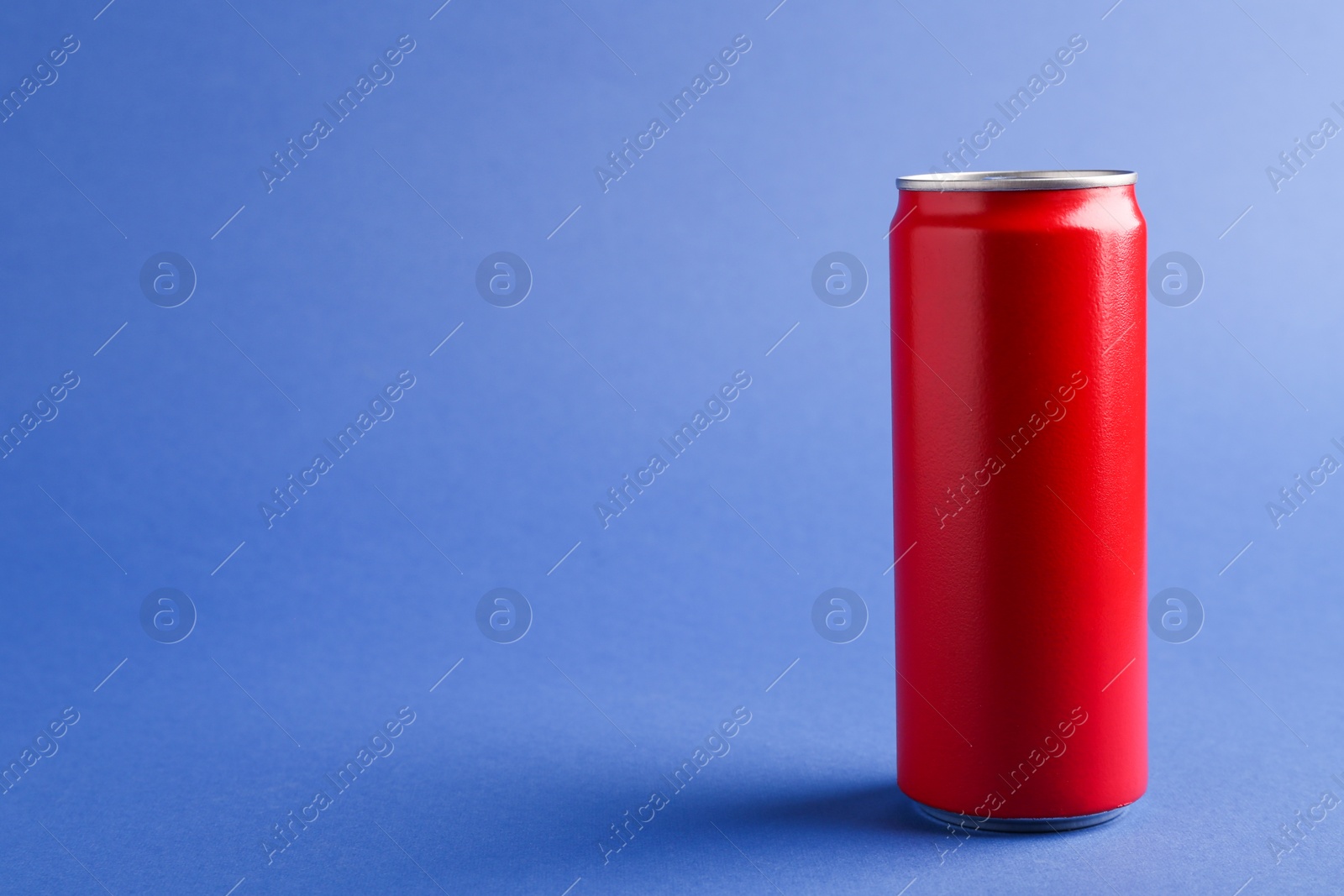 Photo of Energy drink in red can on blue background, space for text