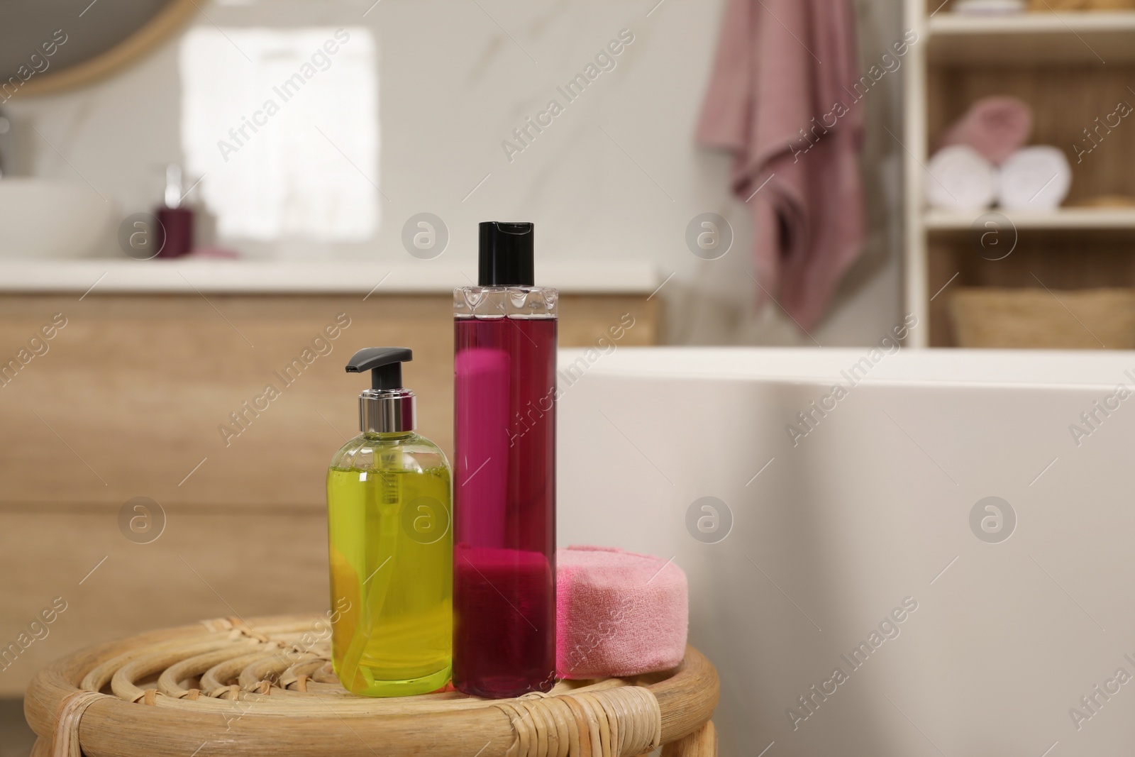 Photo of Bottles of shower gels and sponge on wicker table near tub in bathroom, space for text