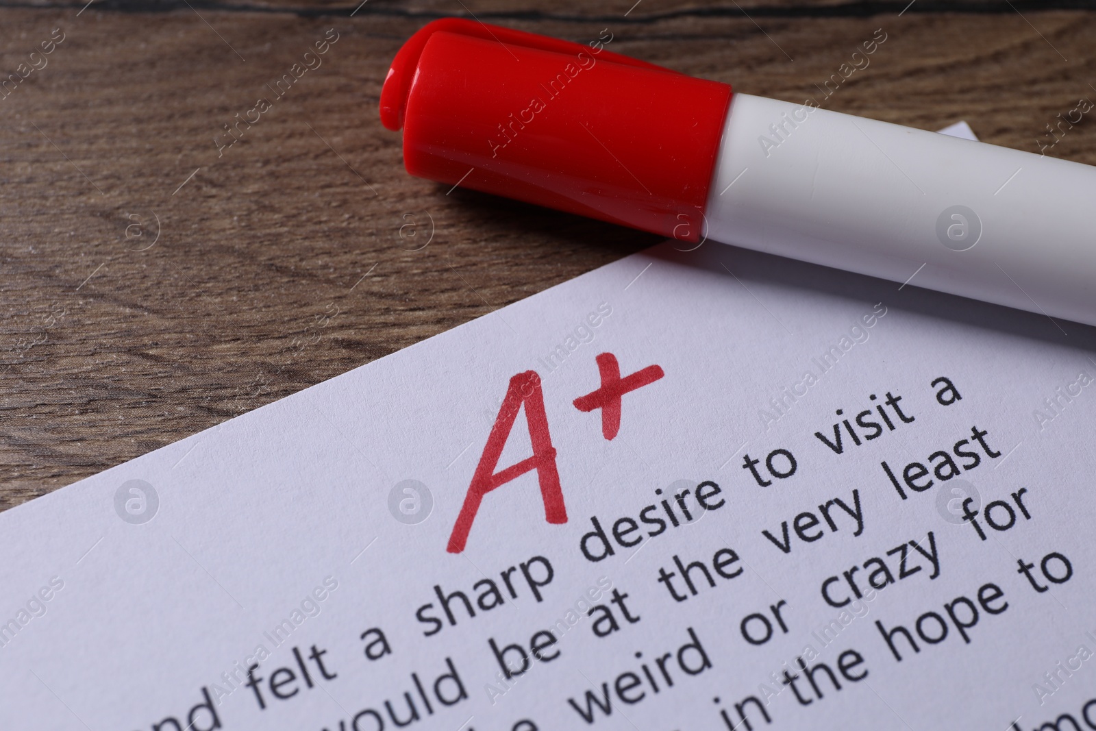 Photo of School grade. Sheet of paper with red letter A, plus symbol and marker on wooden table, closeup