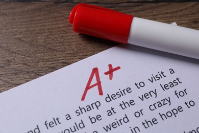 School grade. Sheet of paper with red letter A, plus symbol and marker on wooden table, closeup