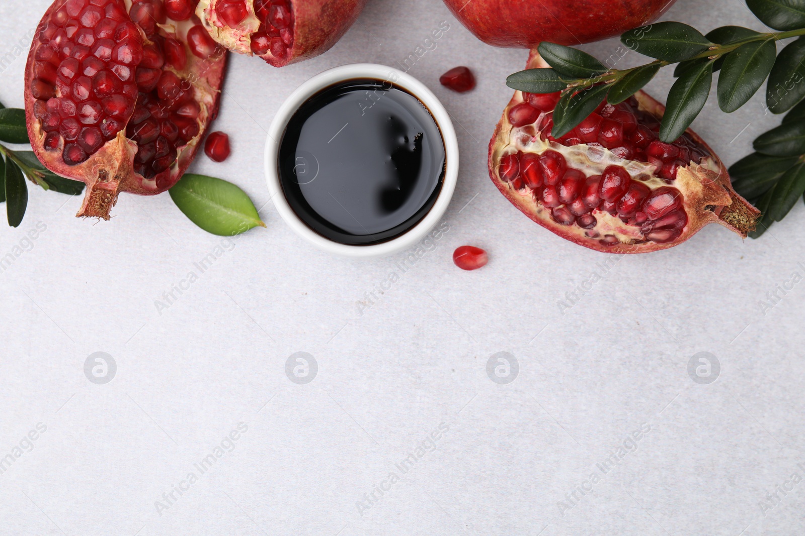 Photo of Tasty pomegranate sauce in bowl, leaves and fruits on light table, flat lay. Space for text