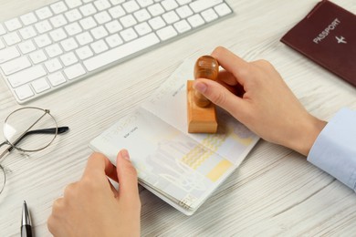 Photo of Moldova, Ceadir-Lunga - June 13, 2022: Woman stamping visa page in passport at white wooden table, closeup