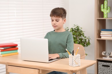 Photo of Boy using laptop at desk in room. Home workplace