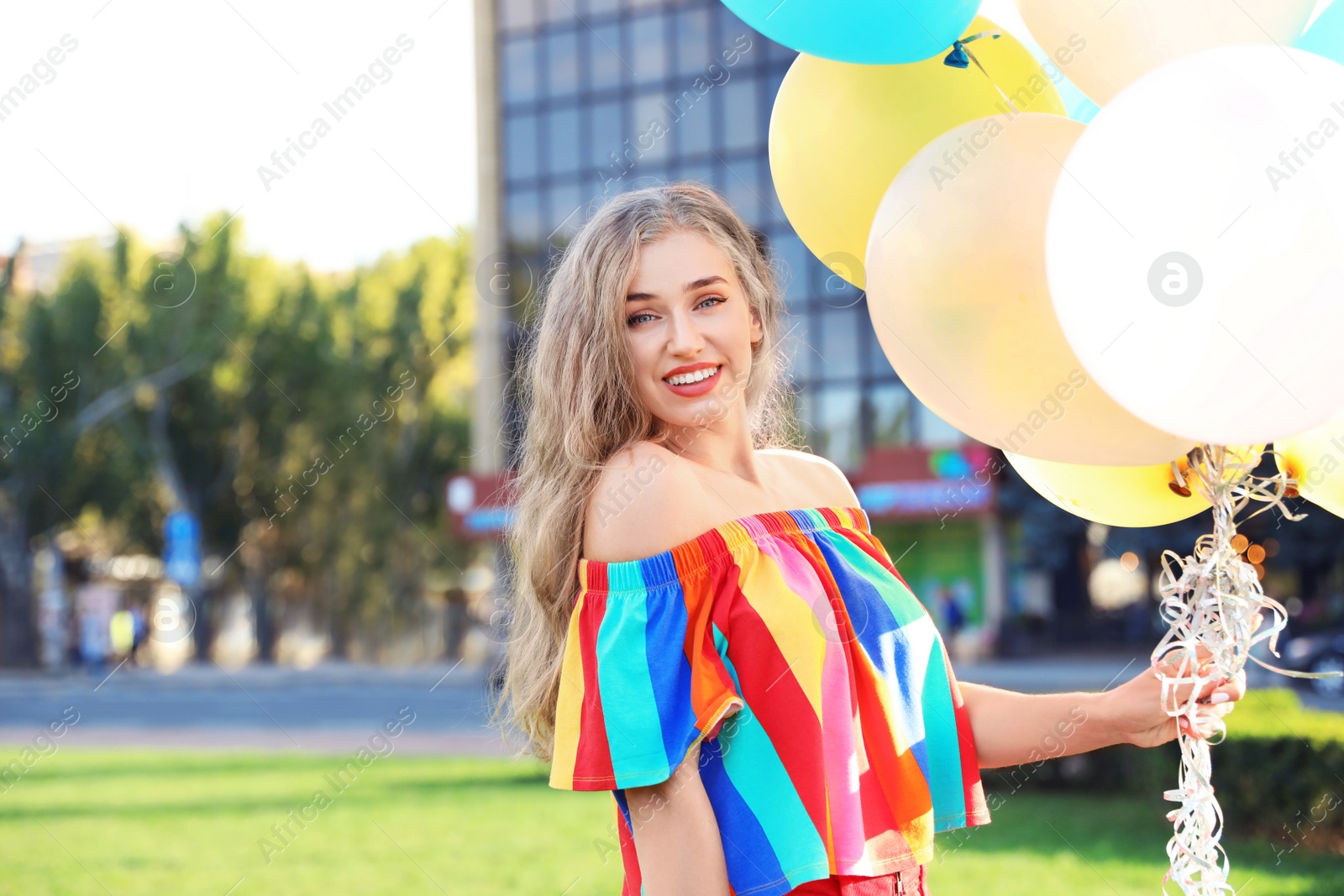 Photo of Beautiful young woman holding colorful balloons on street