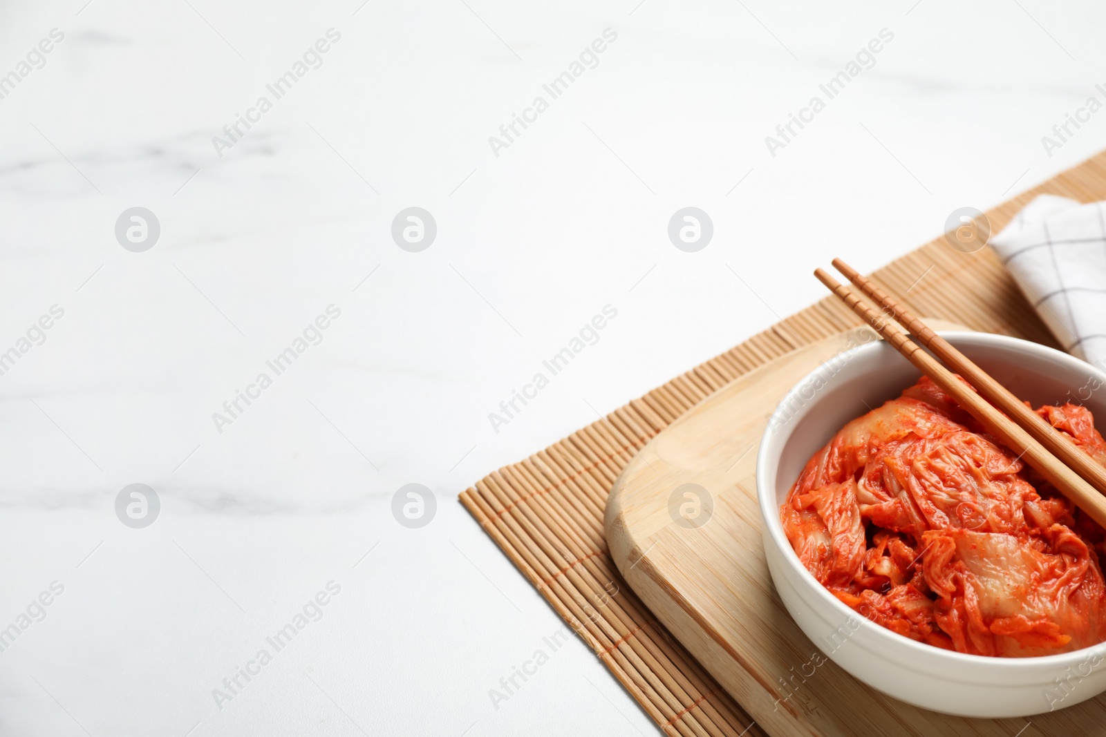 Photo of Bowl of spicy cabbage kimchi with chopsticks on white marble table, space for text