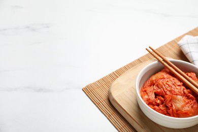 Photo of Bowl of spicy cabbage kimchi with chopsticks on white marble table, space for text