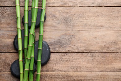Photo of Spa stones and bamboo stems on wooden table, flat lay. Space for text