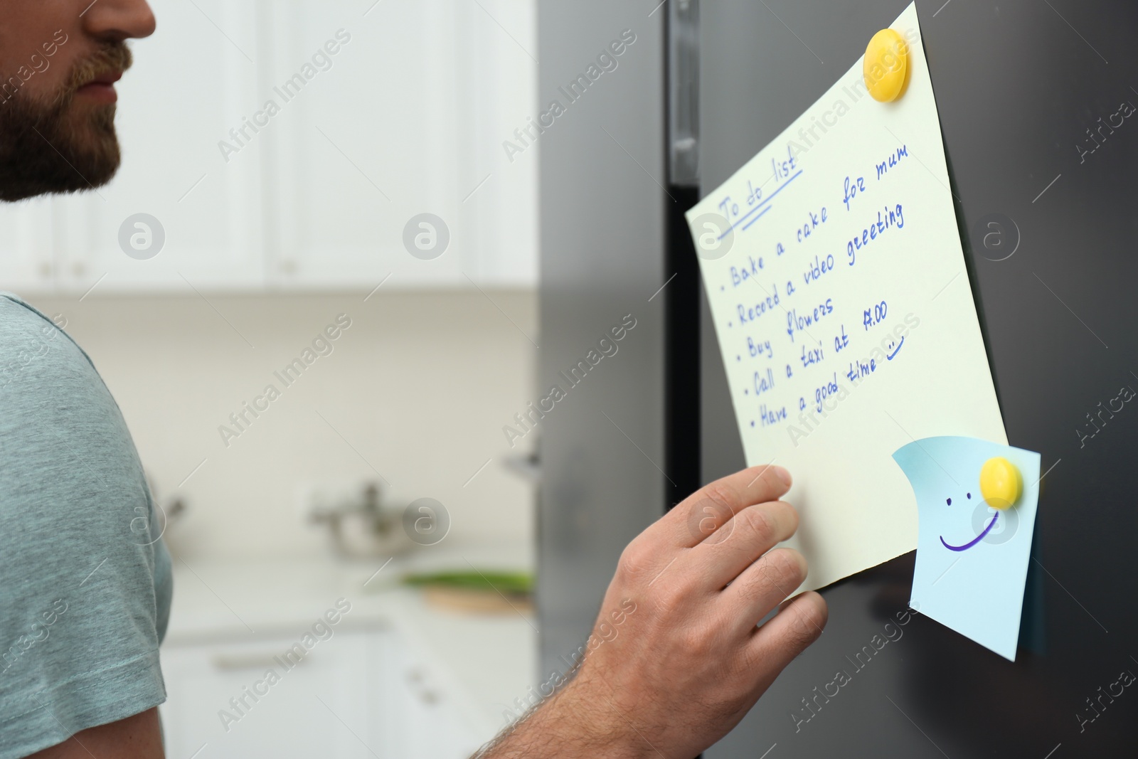 Photo of Man checking to do list on fridge in kitchen, closeup