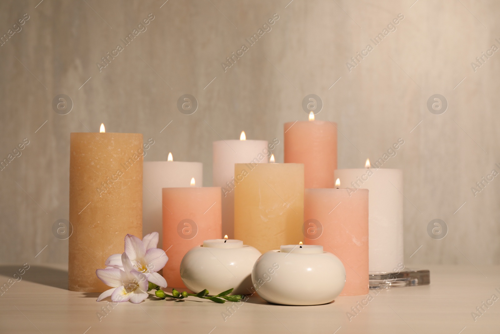 Photo of Burning candles and beautiful flowers on wooden table
